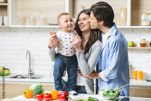 Young family embracing with baby at kitchen, empty space