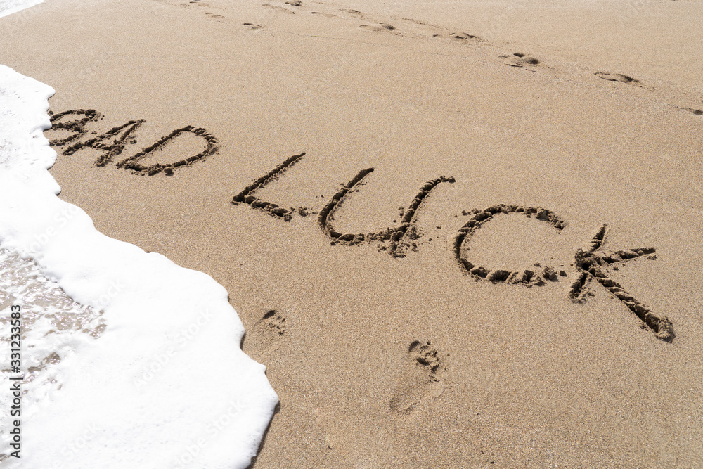 Fototapeta premium English word 'bad luck' written on the sand beach washing away by bubble ocean wave.