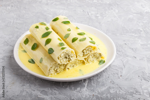 Cannelloni pasta with egg sauce, cream cheese and oregano leaves on a gray concrete background. side view