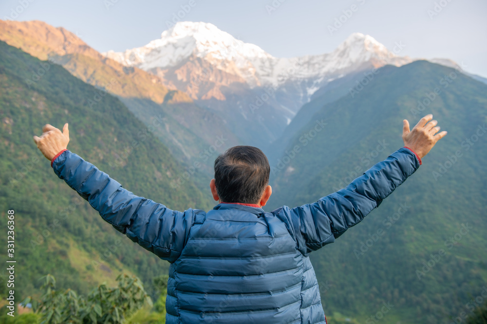 Back view of Middle-aged man raised his hands and looking to beautiful view of Annapurna mountains range in the morning. Annapurna Region is the most diverse and popular trekking area in Nepal. Back view of Middle-aged man raised his hands and looking to beautiful view of Annapurna mountains range in the morning. Annapurna Region is the most diverse and popular trekking area in Nepal.