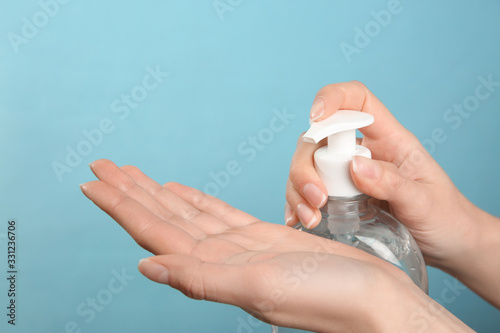 Woman applying antiseptic gel on light blue background  closeup