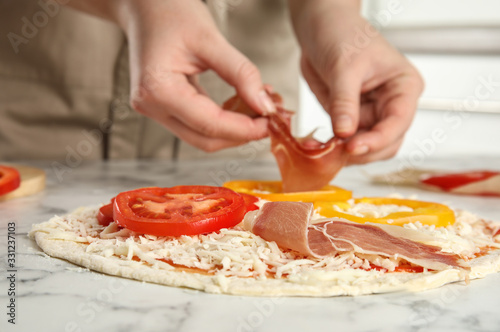 Woman adding prosciutto to pizza white marble table, closeup