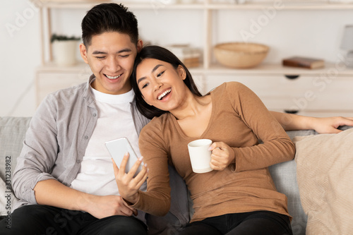 Konstfotografi Asian couple resting on couch, using phone