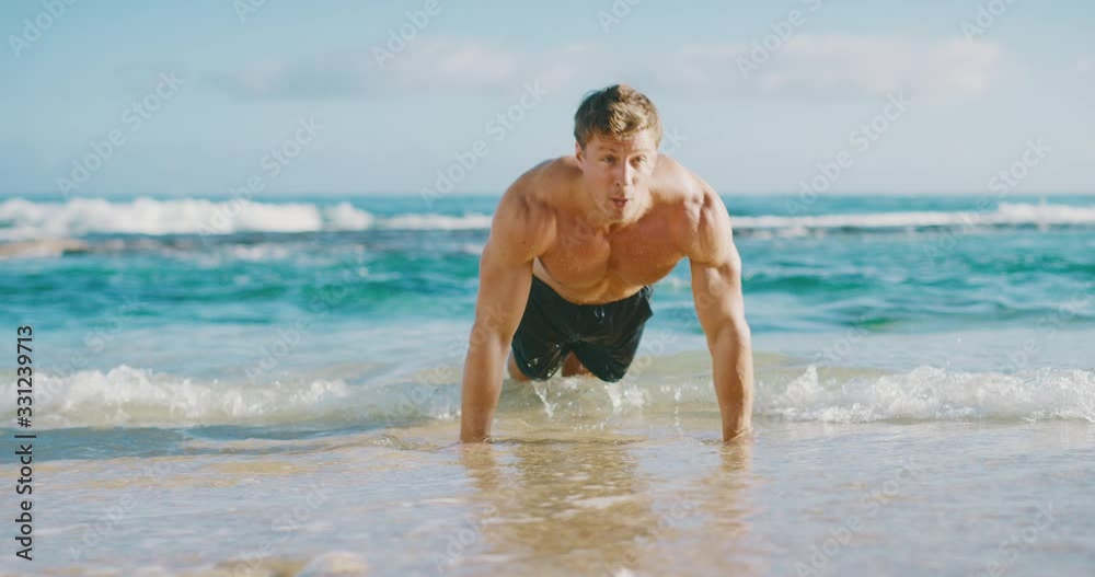 Strong muscular man doing push ups on the beach in the morning, fit young man working out