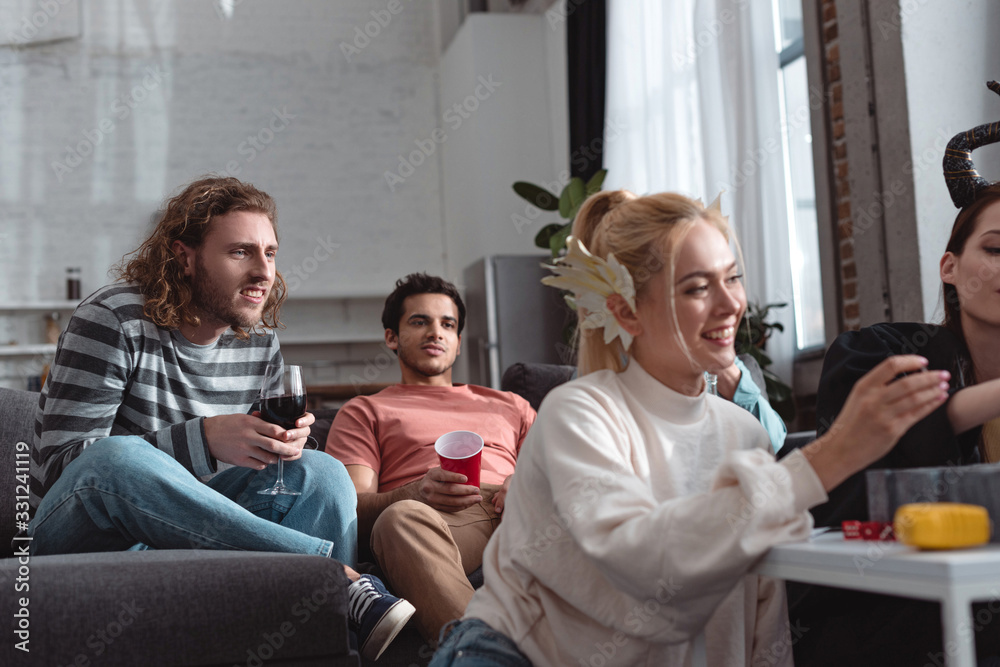 attentive men looking at smiling girls in fairy costumes playing board game