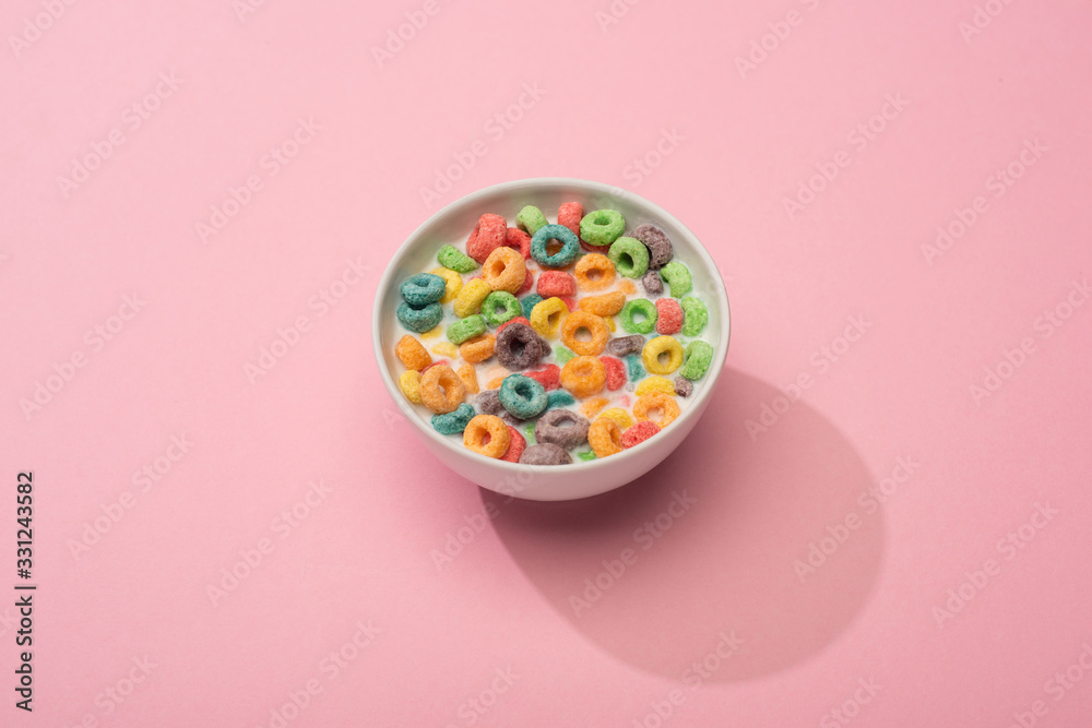 bright colorful breakfast cereal with milk in bowl on pink background