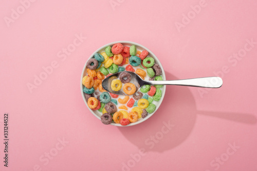 top view of bright colorful breakfast cereal in bowl with spoon on pink background photo