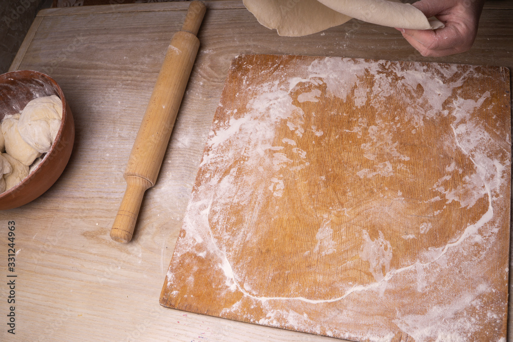 A woman rolls out the dough. Plywood cutting board, wooden flour sieve and wooden rolling pin - tools for making dough. A woman rolls out the dough. Plywood cutting board, wooden flour sieve and wooden rolling pin - tools for making dough.