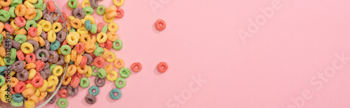 top view of bright colorful breakfast cereal scattered from bowl on pink background, panoramic shot