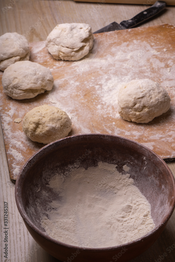 Fototapeta premium Balls of dough. Plywood cutting board, wooden flour sieve and wooden rolling pin - tools for making dough.