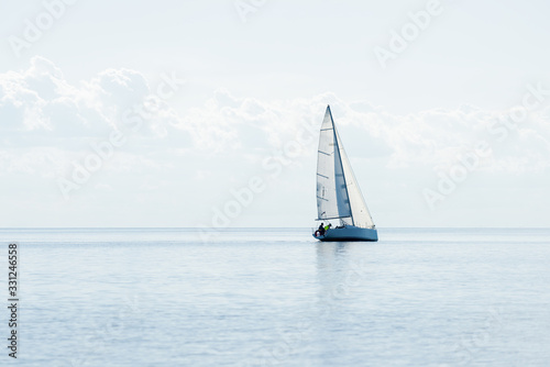 White sloop rigged modern yacht sailing in a Mediterranean sea on a clear sunny day, Spain. Blue sky with white clouds, reflections on water; photo