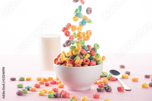 selective focus of bright multicolored breakfast cereal falling in bowl near milk and spoon on white background