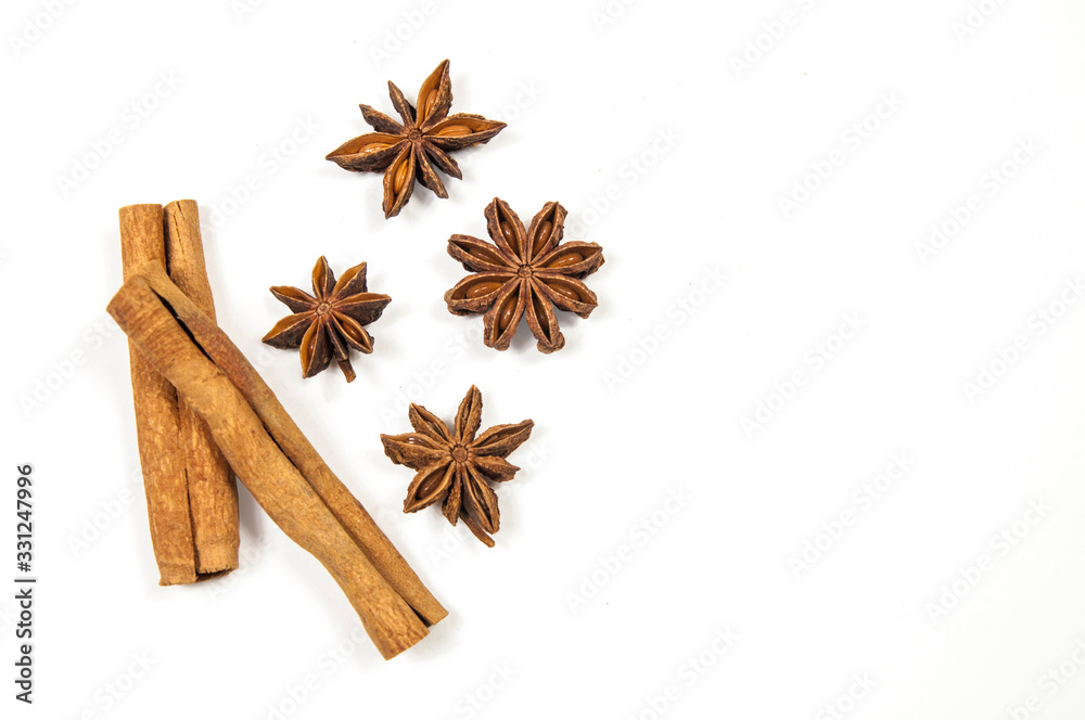 two sticks of cinnamon, one on top of the other,on the right side four stars of star anise on a white background close-up view from above two sticks of cinnamon, one on top of the other,on the right side four stars of star anise on a white background close-up view from above