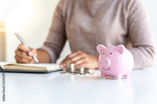 Young business women are saving money in a piggy bank and recording financial income-expenditures to prepare investments in real estate, Tax deduction and cost calculation concept.