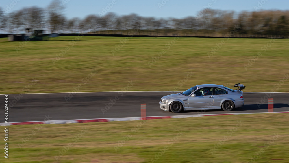 A panning shot of  a silver car cornering.