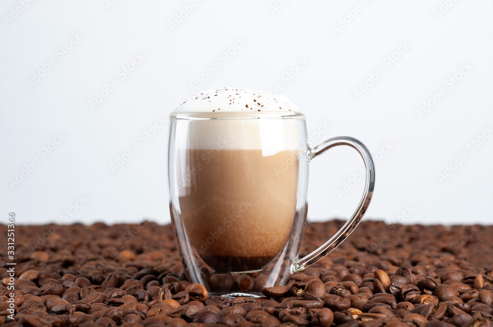 a transparent cup of latte with cinnamon on a foam with a double bottom stands among coffee beans on a white background. Copyspace a transparent cup of latte with cinnamon on a foam with a double bottom stands among coffee beans on a white background. Copyspace