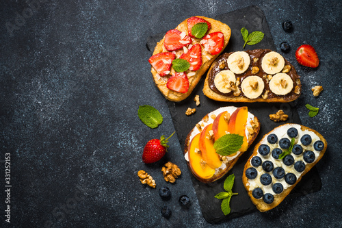 Sweet toast assortment with fresh fruit and berries on black.