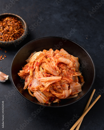 Kimchi cabbage in a black ceramic bowl on a black background. Place for text, top view. Korean food