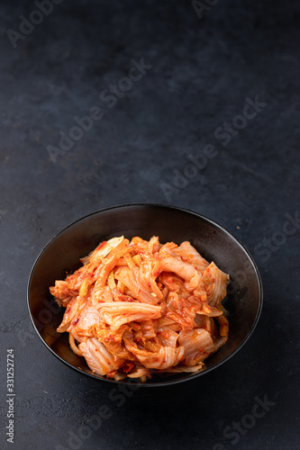 Kimchi cabbage in a black ceramic bowl on a black background. Place for text, top view. Korean food