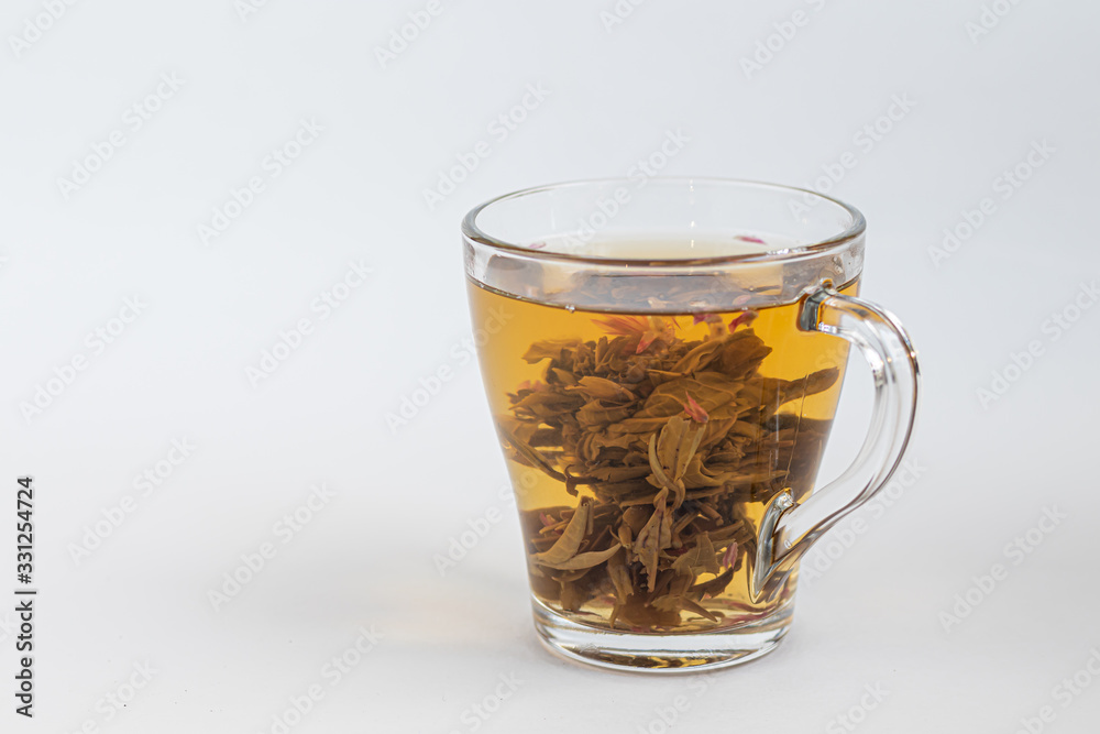 Blooming green tea in a glass teapot. On a light surface. Nearby are tea briquettes of leaves and flowers. Blooming green tea in a glass teapot. On a light surface. Nearby are tea briquettes of leaves and flowers.