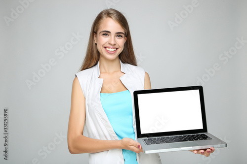 Beautiful woman holding laptop computer on grey background