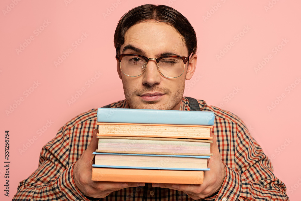 winking male nerd in eyeglasses holding books, Isolated on pink winking male nerd in eyeglasses holding books, Isolated on pink