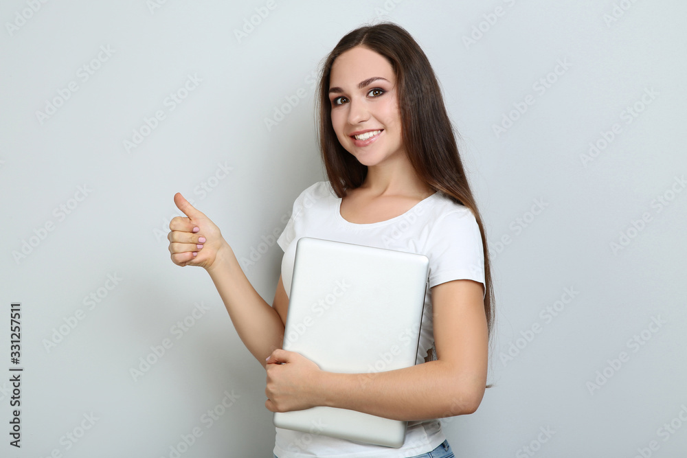 Young girl with laptop computer showing thumb up on grey background Young girl with laptop computer showing thumb up on grey background