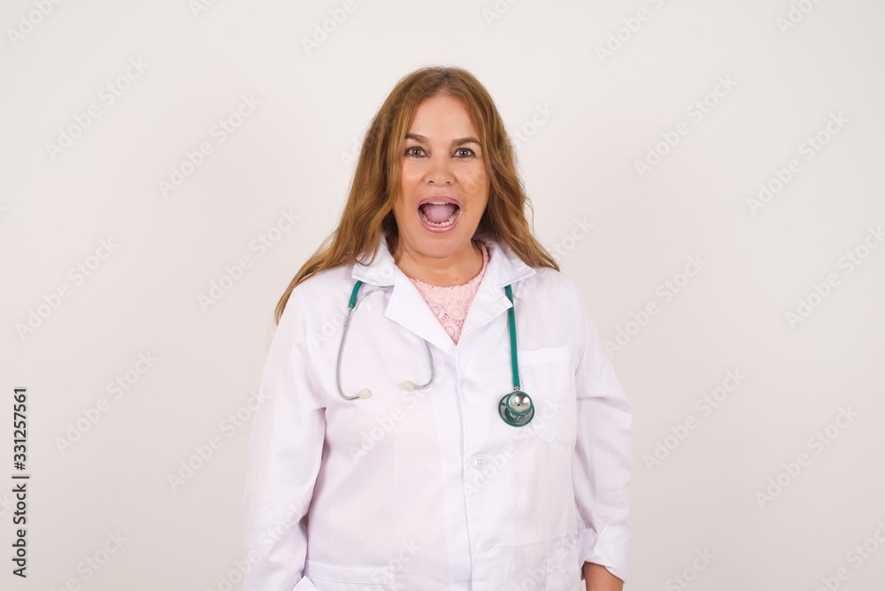 Emotive young doctor woman wearing medical uniform, being happy and excited to celebrate anniversary. Happy young woman has good mood stands indoor. Emotive young doctor woman wearing medical uniform, being happy and excited to celebrate anniversary. Happy young woman has good mood stands indoor.