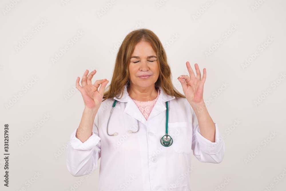 Meditation, religion and spiritual practices. Beautiful young doctor female doing yoga in the morning before work, keeping eyes closed, holding fingers in mudra gesture. Meditation, religion and spiritual practices. Beautiful young doctor female doing yoga in the morning before work, keeping eyes closed, holding fingers in mudra gesture.