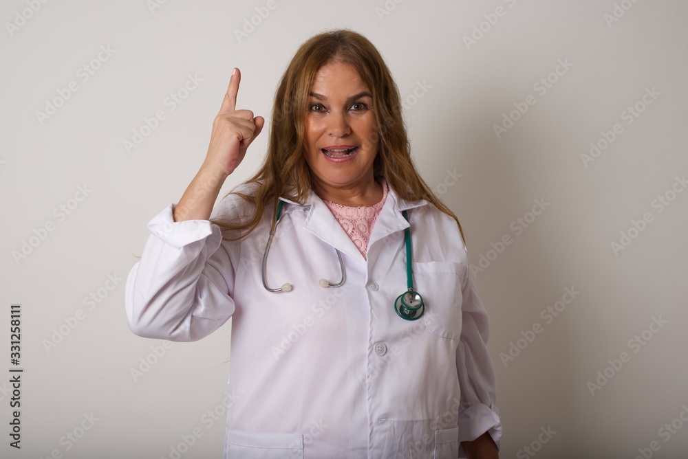 Close-up portrait of charming young doctor woman in medical uniform pointing with one finger up, looking up and smiling, I have an idea, I know the answer or the solution. Close-up portrait of charming young doctor woman in medical uniform pointing with one finger up, looking up and smiling, I have an idea, I know the answer or the solution.