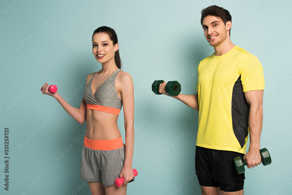 cheerful athletic couple training with dumbbells on blue cheerful athletic couple training with dumbbells on blue