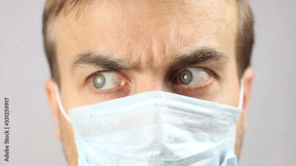 close-up front view on male face in medical mask, looks around with fear and distrust, quarantine or epidemic of virus or protection of pollution, gray background close-up front view on male face in medical mask, looks around with fear and distrust, quarantine or epidemic of virus or protection of pollution, gray background
