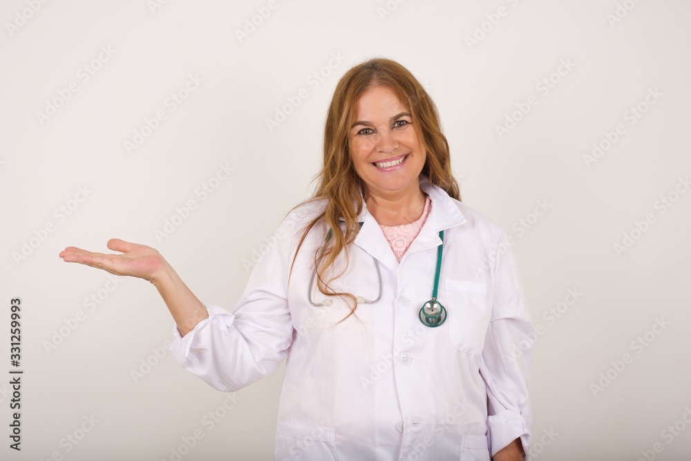 Positive glad doctor female says: wow how exciting it is, has amazed expression, shows something on blank space with open hand over isolated gray background. Advertisement concept. Positive glad doctor female says: wow how exciting it is, has amazed expression, shows something on blank space with open hand over isolated gray background. Advertisement concept.