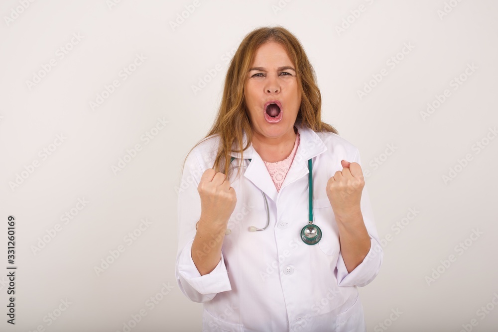 Waist up portrait of successful determined young doctor female wearing medical uniform clenching fists, exclaiming GOAL with joy and excitement. Victory, success and achievement concept. Waist up portrait of successful determined young doctor female wearing medical uniform clenching fists, exclaiming GOAL with joy and excitement. Victory, success and achievement concept.