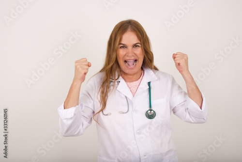Waist up portrait of strong successful determined young doctor woman wearing medical uniform  clenching fists  exclaiming with joy and excitement. Victory  success and achievement concept.