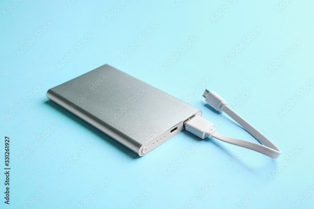 Modern portable charger with cable on light blue background Modern portable charger with cable on light blue background