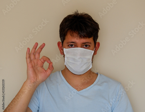 COVID-19 Pandemic Coronavirus; Man wearing face mask protective for spreading of Coronavirus Disease and and making OK gesture. Portrait of man with surgical mask on face against SARS-CoV-2.