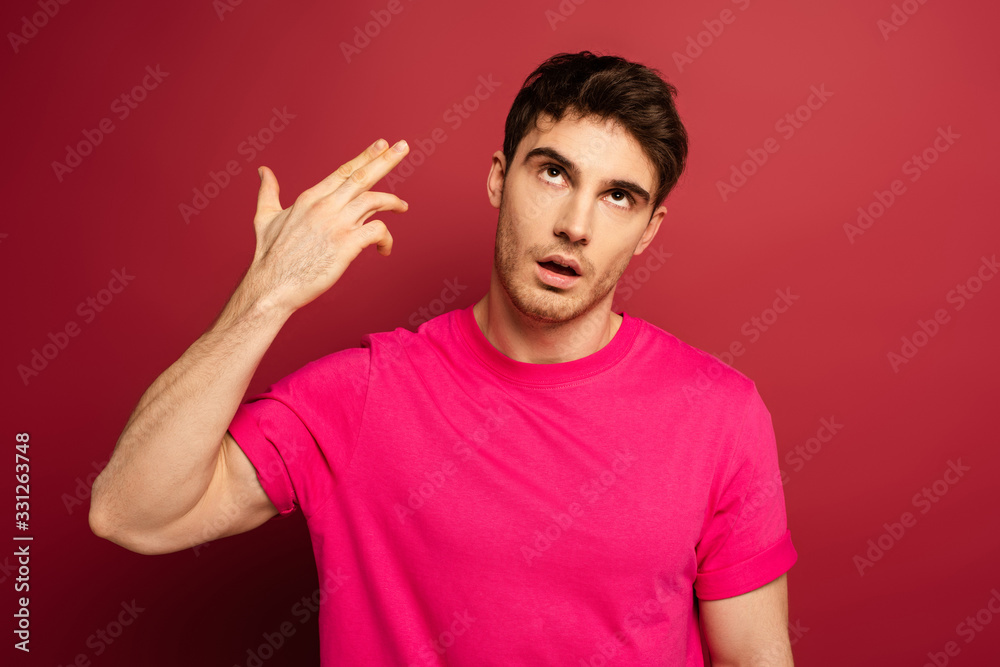portrait of frustrated man in pink t-shirt with hand gun gesture on red portrait of frustrated man in pink t-shirt with hand gun gesture on red