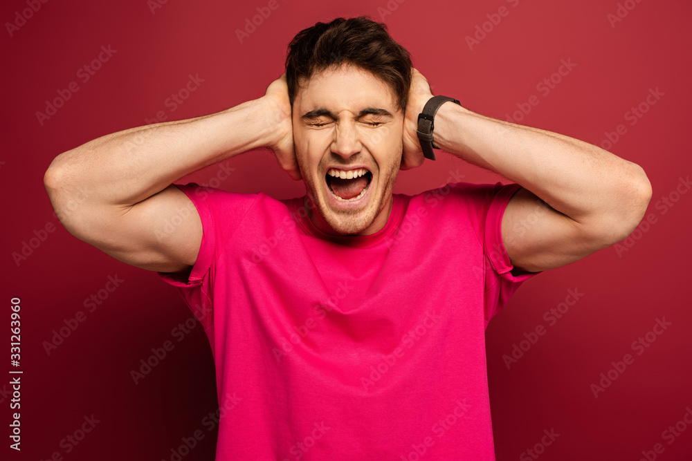 Portrait of smiling man shouting and covering ears on red Portrait of smiling man shouting and covering ears on red