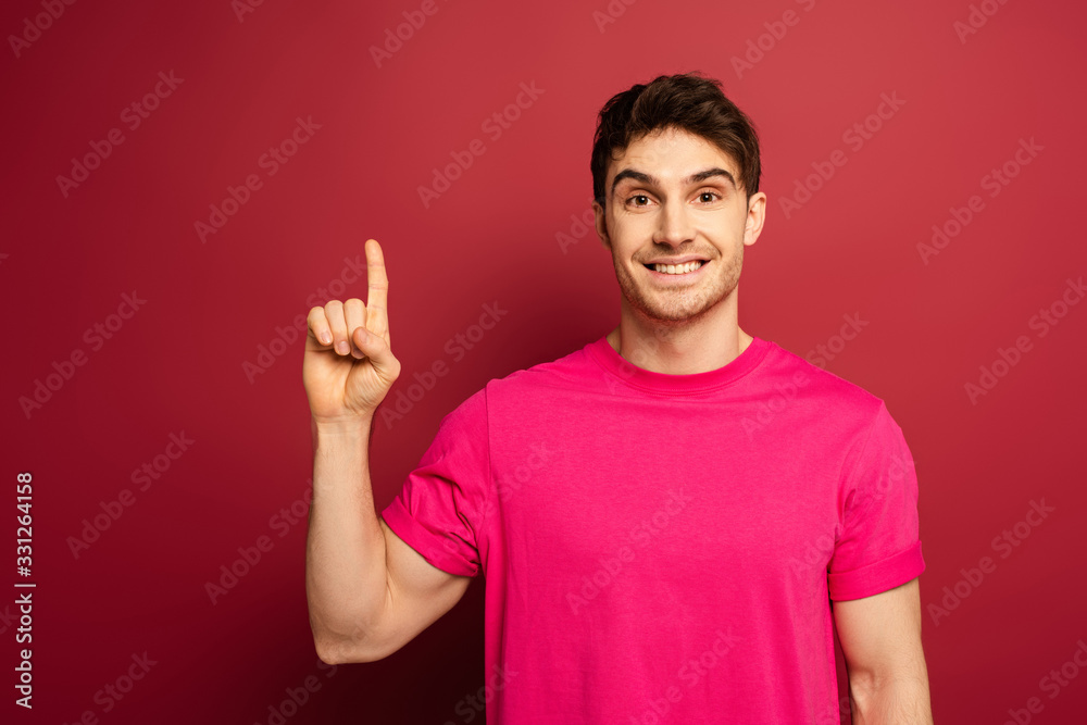 portrait of smiling man in pink t-shirt pointing up on red portrait of smiling man in pink t-shirt pointing up on red