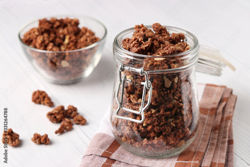 Chocolate Granola crispy muesli with natural honey and nuts in a glass jar and bowl against a white background, healthy food, Horizontal format Chocolate Granola crispy muesli with natural honey and nuts in a glass jar and bowl against a white background, healthy food, Horizontal format