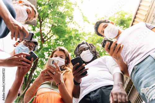 Group of young people of different ethnicities standing together with a mobile phone in hand wearing protective masks