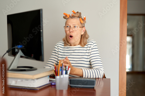Woman with curlers on her head looks at a computer screen.