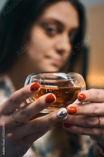 A girl with outstretched arms holds a transparent bowl with black tea.