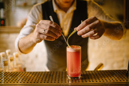 Tablou pe pânză barmen preparing rhubarb cocktail in highball glass and holding slice of rhubarb