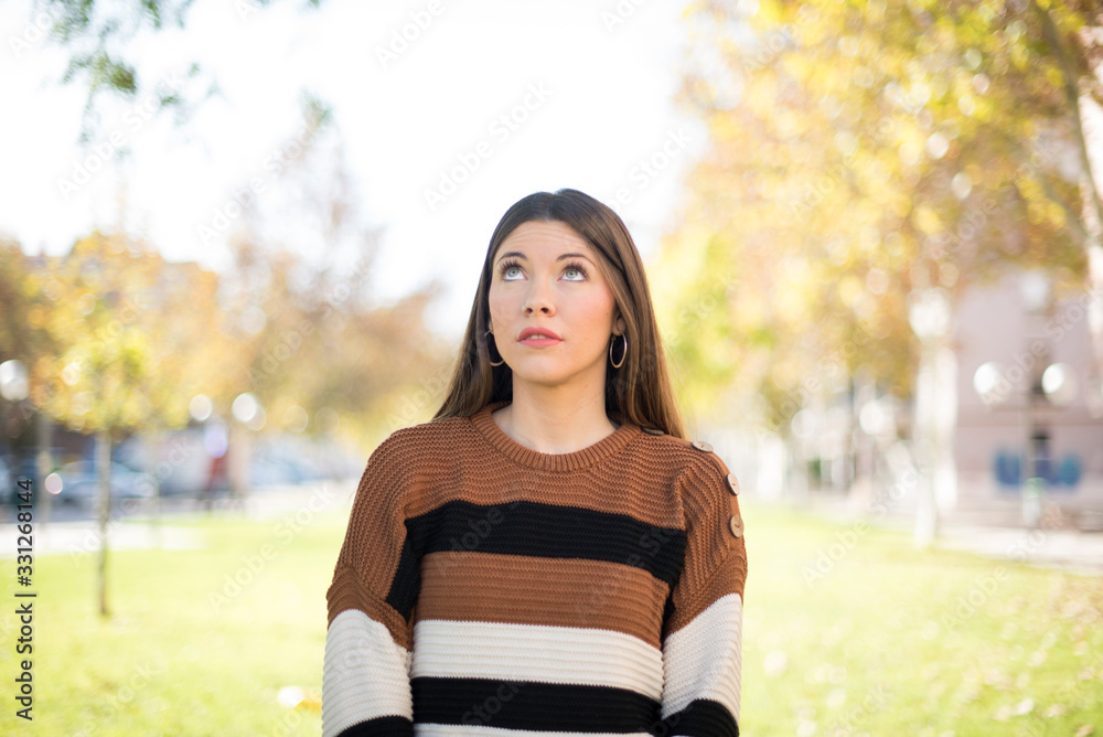 portrait of mysterious charming female with straight hair looking up with enigmatic smile. Beautiful smiling girl looking up standing against gray wall. portrait of mysterious charming female with straight hair looking up with enigmatic smile. Beautiful smiling girl looking up standing against gray wall.