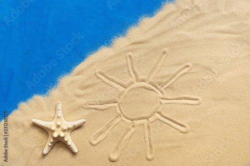 Drawn sun on the sea sand and starfish on a blue painted background. Vacation and travel concept. Studio shot.
