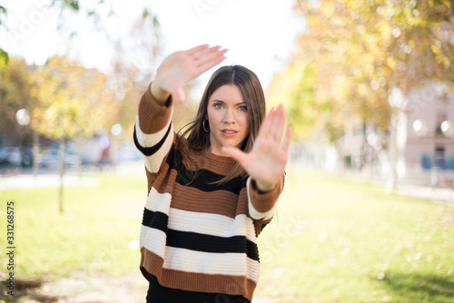 Gesturing finger frame. Portrait of smiling beautiful young woman looking at camera and gesturing finger frame while standing outdoors in a park.