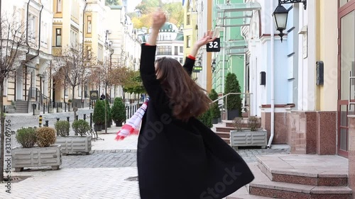 Young woman spinning holding her hands up joyfully in a black coat in the city. Stock footage. Slow motion