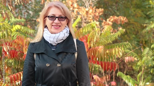 Cheerful mature woman in glasses smiling. Adult long-haired blonde woman in trench coat smiling. Outdoors. Older people and communication conceptt.